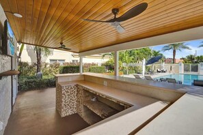 Ein Poolbereich im Freien mit Holzdecke, einer integrierten Bar und Liegestühlen.