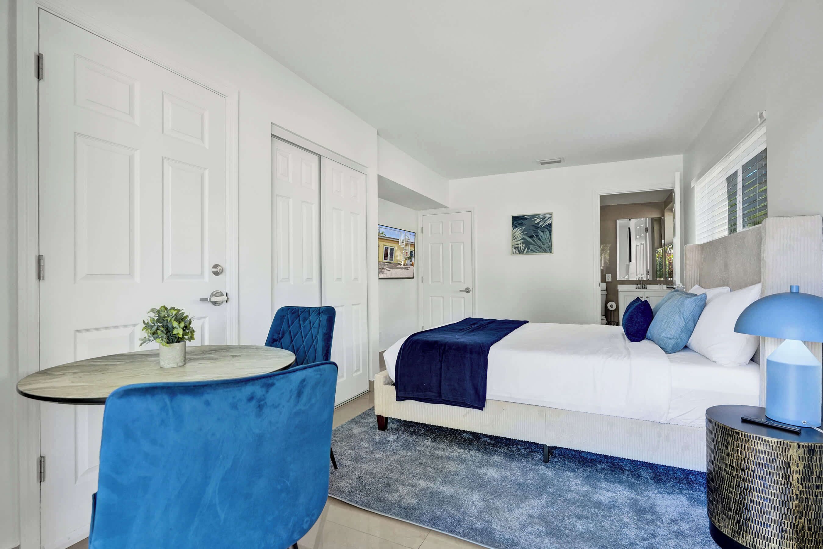 A bedroom with a bed, bedside table, lamp, and a view of the outside.