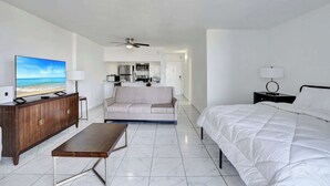 Et hotelværelse med seng, sofa, fjernsyn, skrivebord og tekøkken.