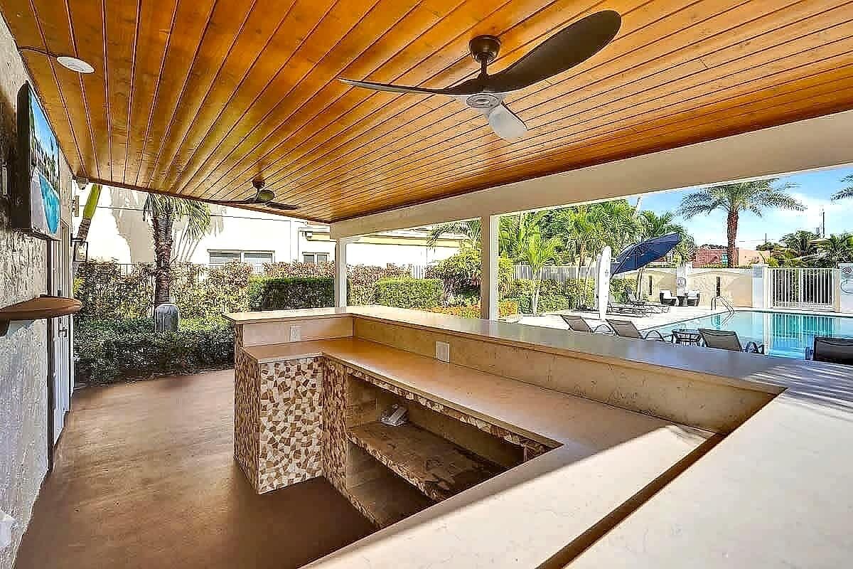 An outdoor bar area with a pool view, ceiling fans, and a tiled backsplash.