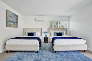 Une chambre d’hôtel avec deux lits, un tapis bleu, un climatiseur, une lampe et un tableau au mur.
