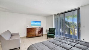 Een slaapkamer met een bed, een dressoir, een televisie, een stoel en een balkon met uitzicht.
