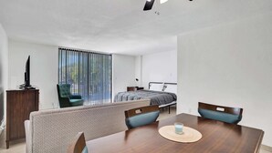 Een moderne hotelkamer met een zithoek, een bed, een televisie en een raam met luxaflex.