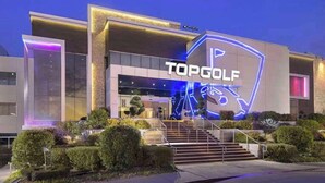 Een modern gebouw met een bord waarop 'TOPGOLF' staat en een neonreclame boven de ingang.