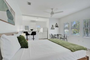 A hotel room with a bed, a desk, a chair, a small kitchen area, and a ceiling fan. - Bright Studio Retreat w/ Kitchen at Lake Worth (Lake Worth Beach)