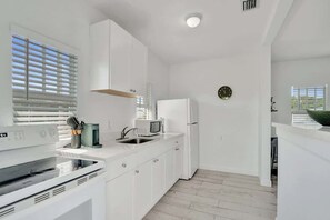A modern kitchen with white cabinetry, a microwave, a refrigerator, and a built-in oven. - Bright Studio Retreat w/ Kitchen at Lake Worth (Lake Worth Beach)