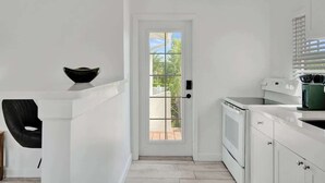A modern kitchen with white cabinetry, a black chair, and a view through a glass door. - Bright Studio Retreat w/ Kitchen at Lake Worth (Lake Worth Beach)