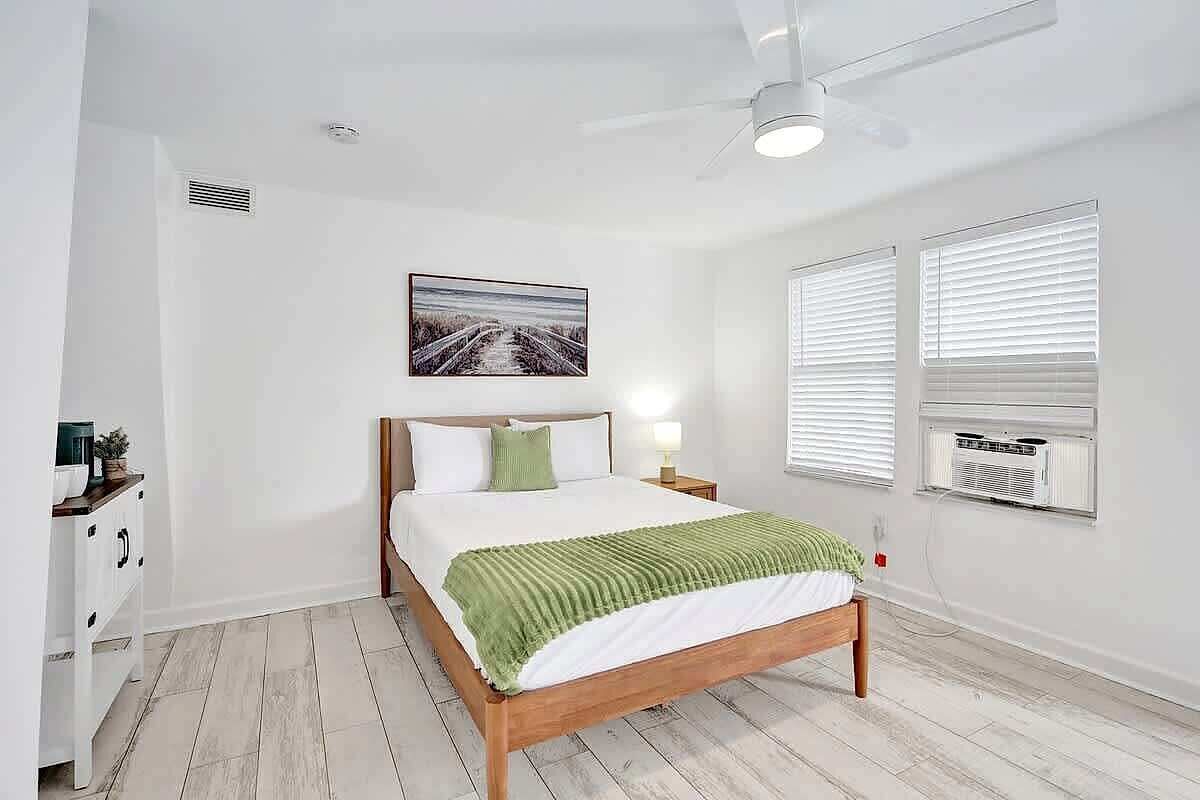 Un dormitorio con una cama, una mesita de noche, aire acondicionado de pared y ventilador de techo.