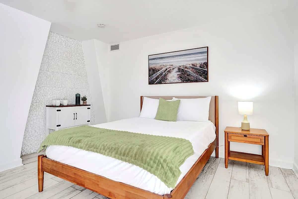 A bedroom with a bed, a nightstand, a wall-mounted picture, and a white wardrobe.