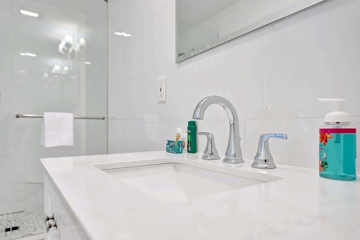 Une salle de bain moderne avec un lavabo blanc, deux robinets et un miroir au-dessus.