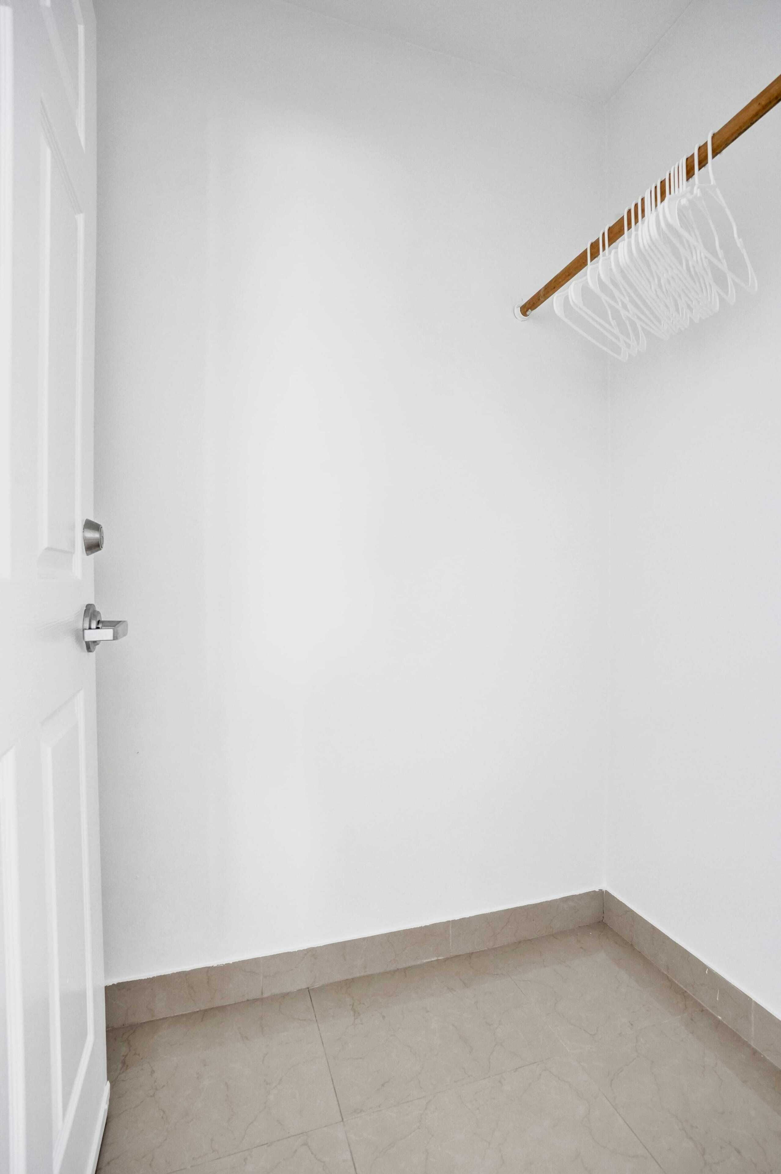 Ein Teil eines Raumes mit weißen Wänden, einem gefliesten Boden und einer Holztür mit einem Metallgriff.
