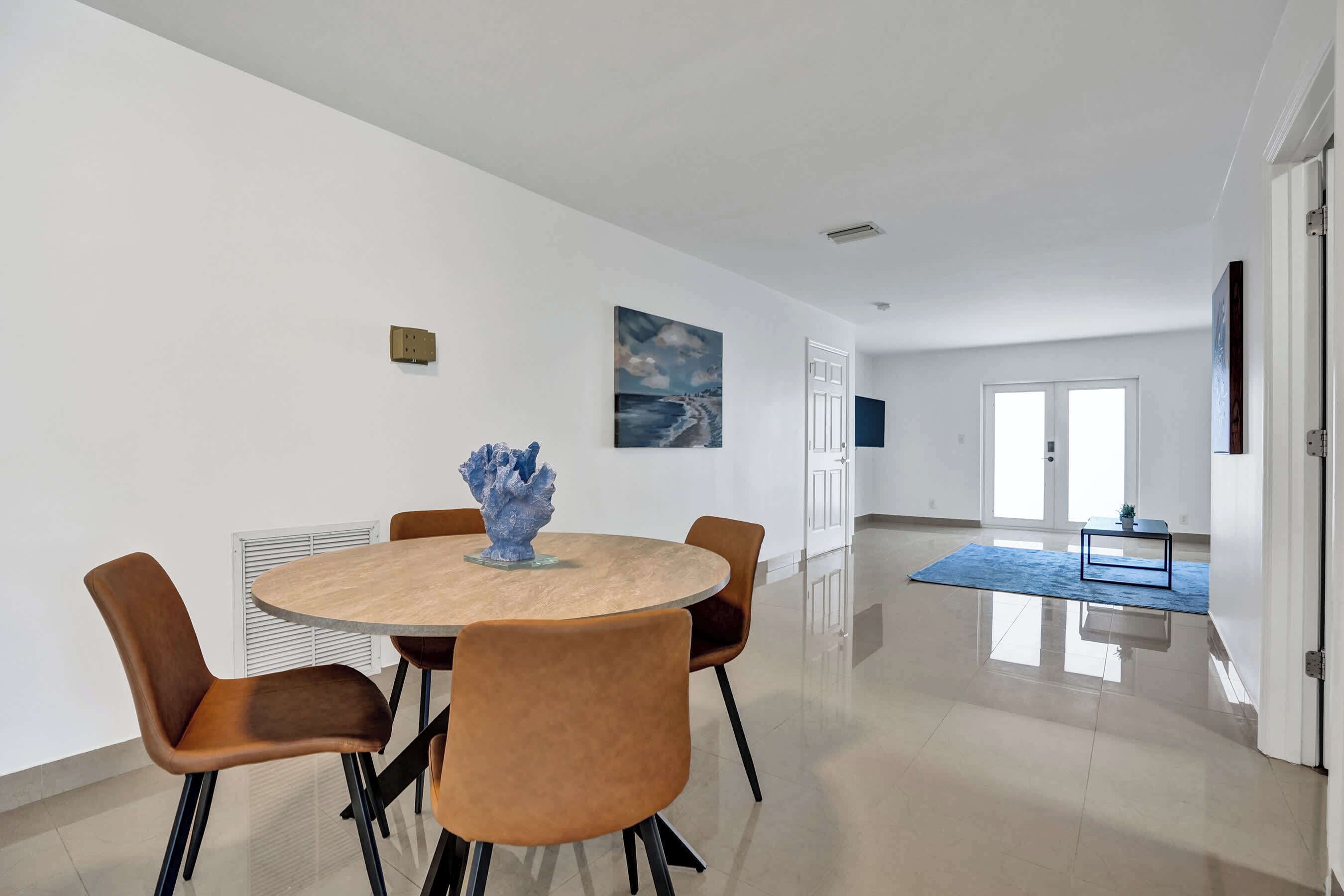A modern dining area with a round table, six chairs, a decorative centerpiece, and a painting on the wall.