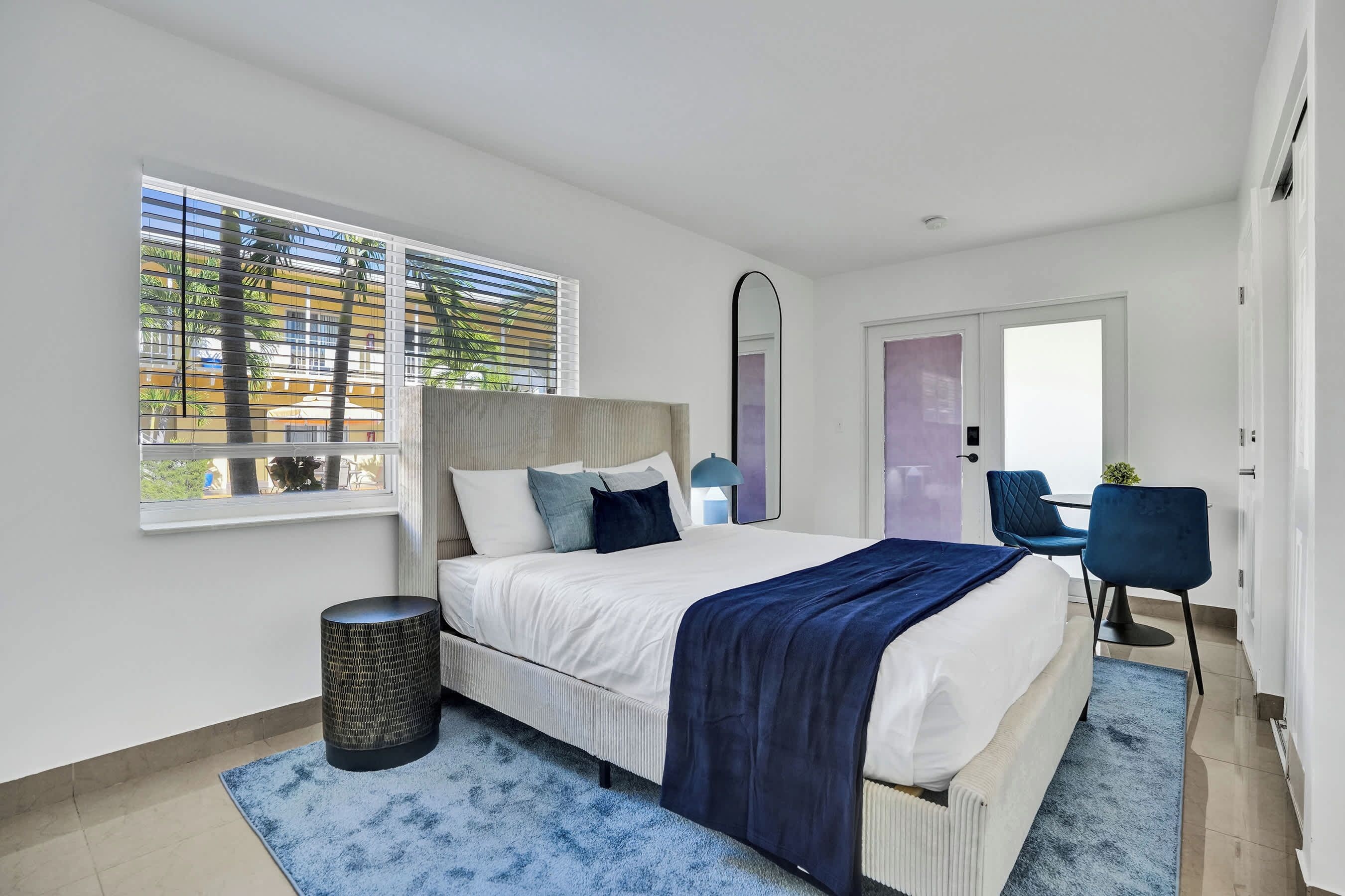 Une chambre moderne avec un grand lit, une table de chevet, une lampe, une chaise et une fenêtre avec des stores.