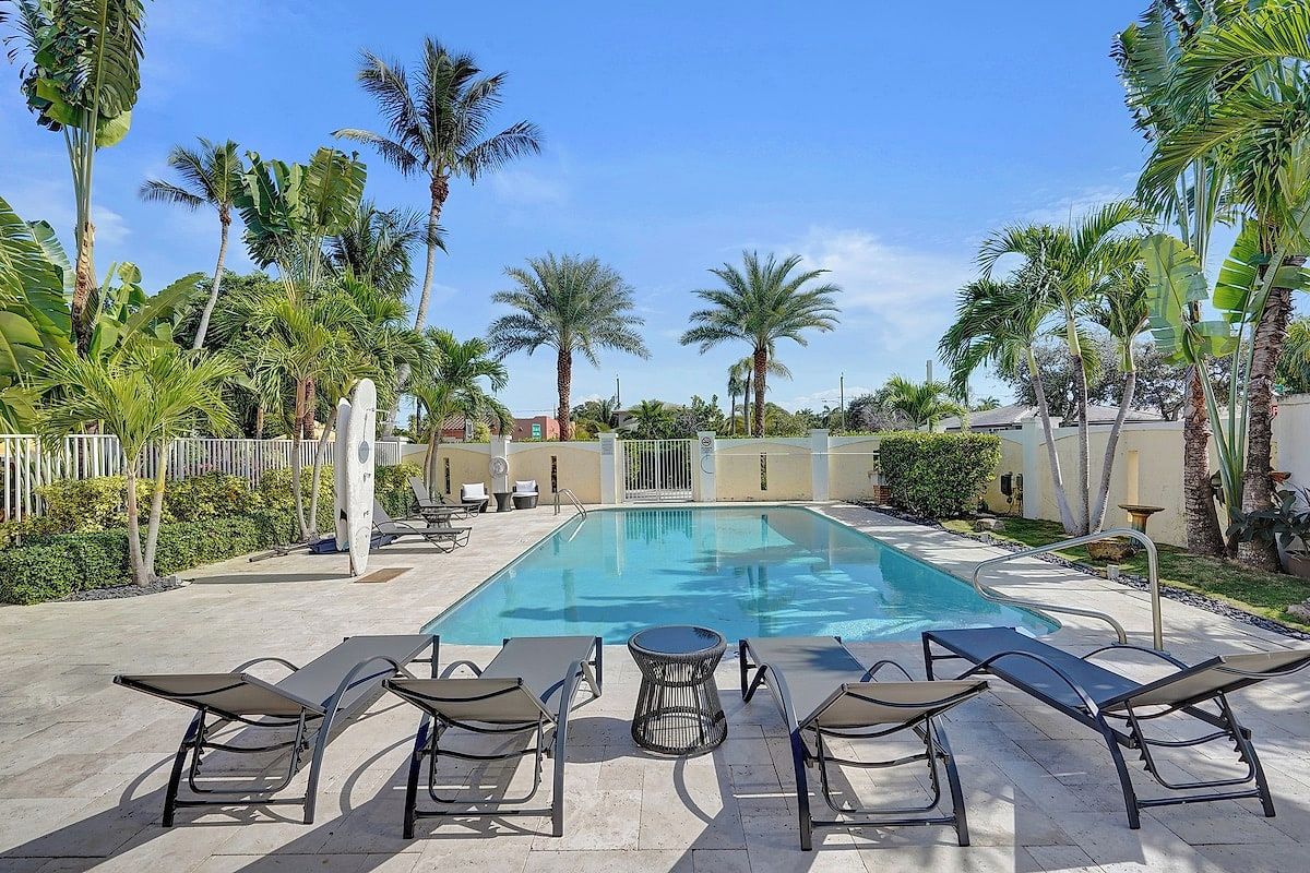 Capri, Lake Worth Beach — community pool with loungers, mature palms, lush landscaping, and clear shallow water.