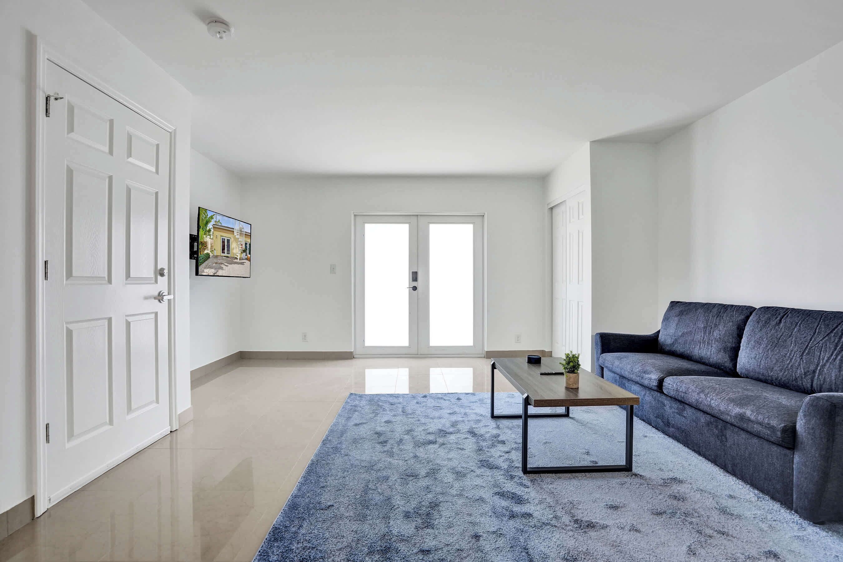 Un salon spacieux avec un canapé gris, une table basse et un tapis bleu.