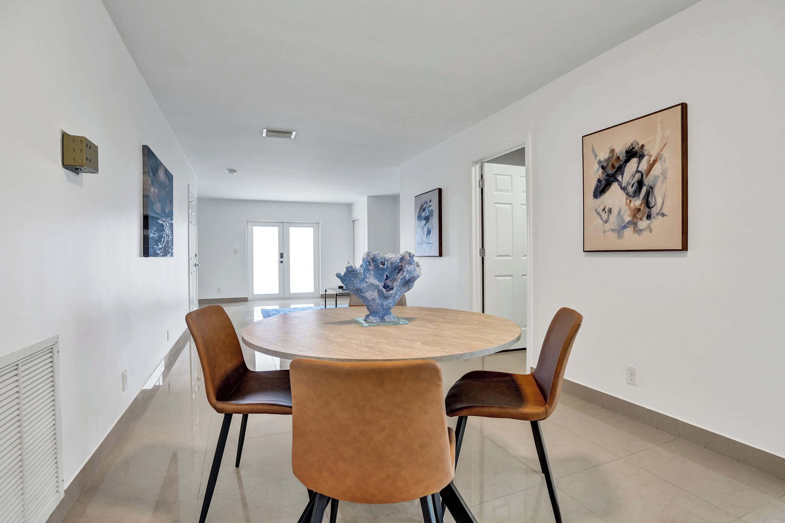 A modern dining area with a round table, two brown chairs, and a decorative centerpiece.