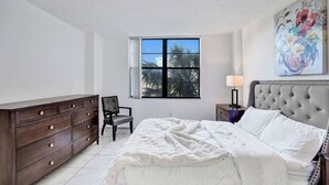 Een slaapkamer met een bed, een kaptafel, een stoel, een raam en kunstwerken.