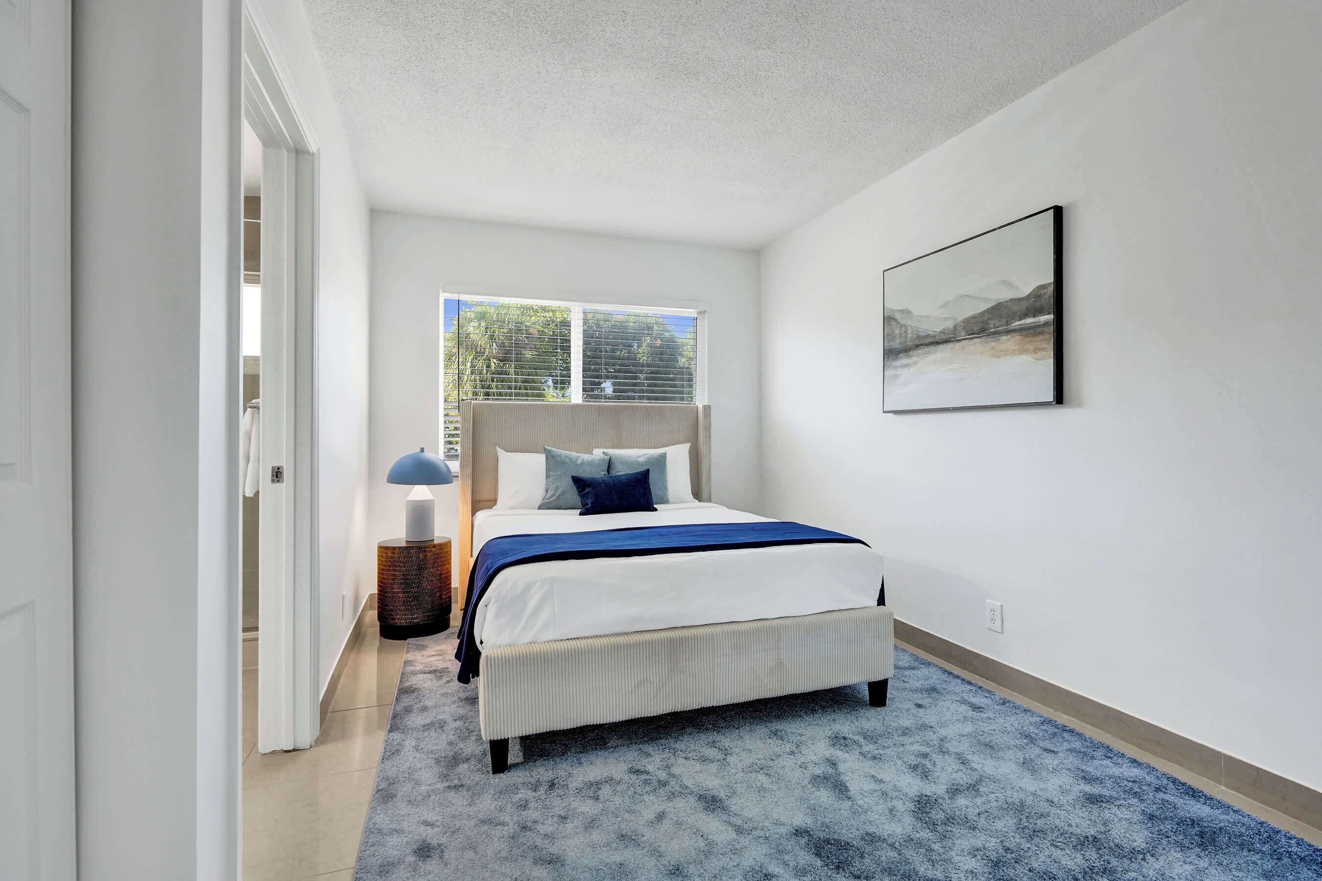 A bedroom with a bed, a window, a picture on the wall, and a door leading to another room.