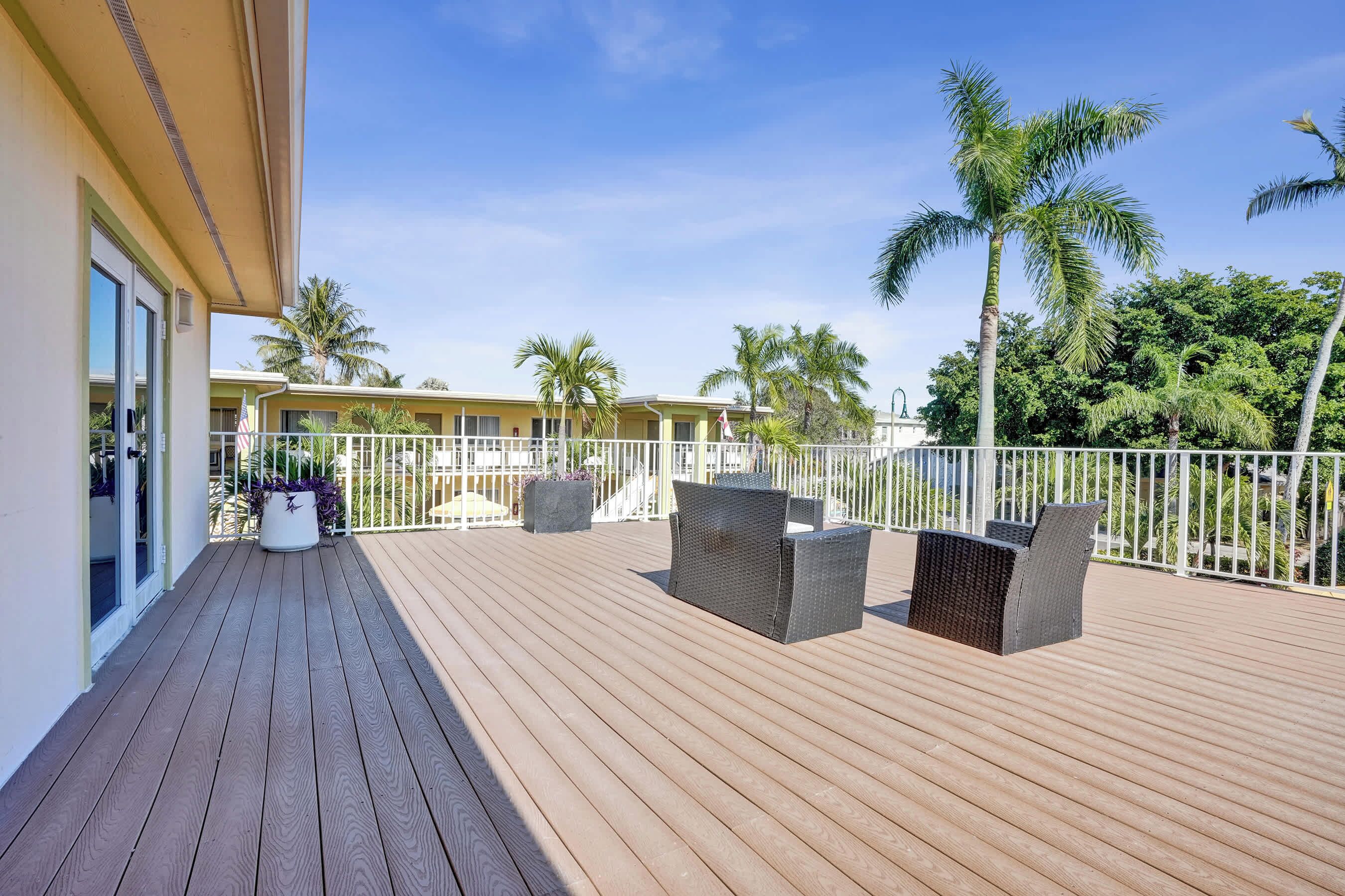 A wooden deck with outdoor furniture, a white railing, and palm trees.