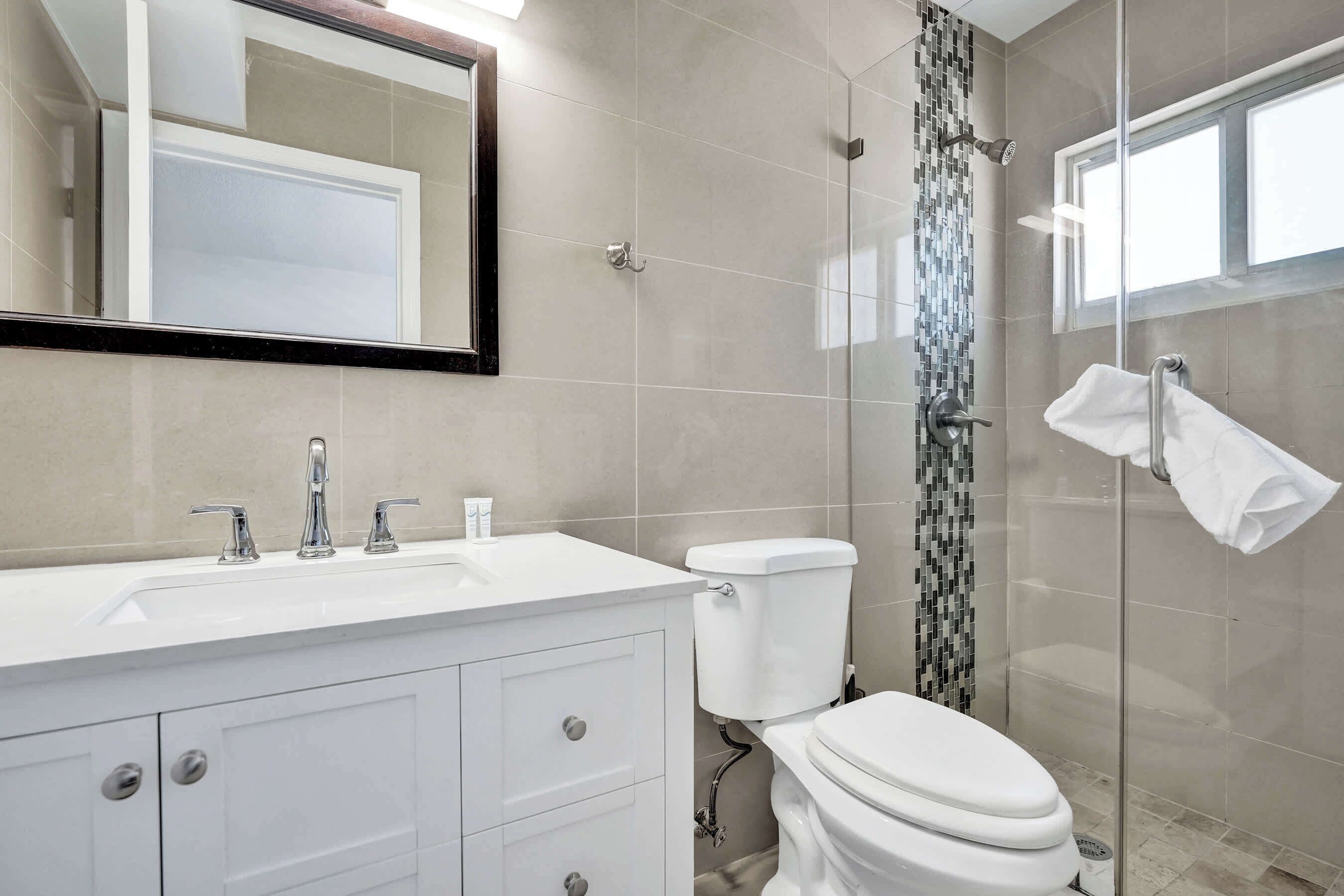 Une salle de bain avec un lavabo blanc, un miroir, des toilettes et une douche.