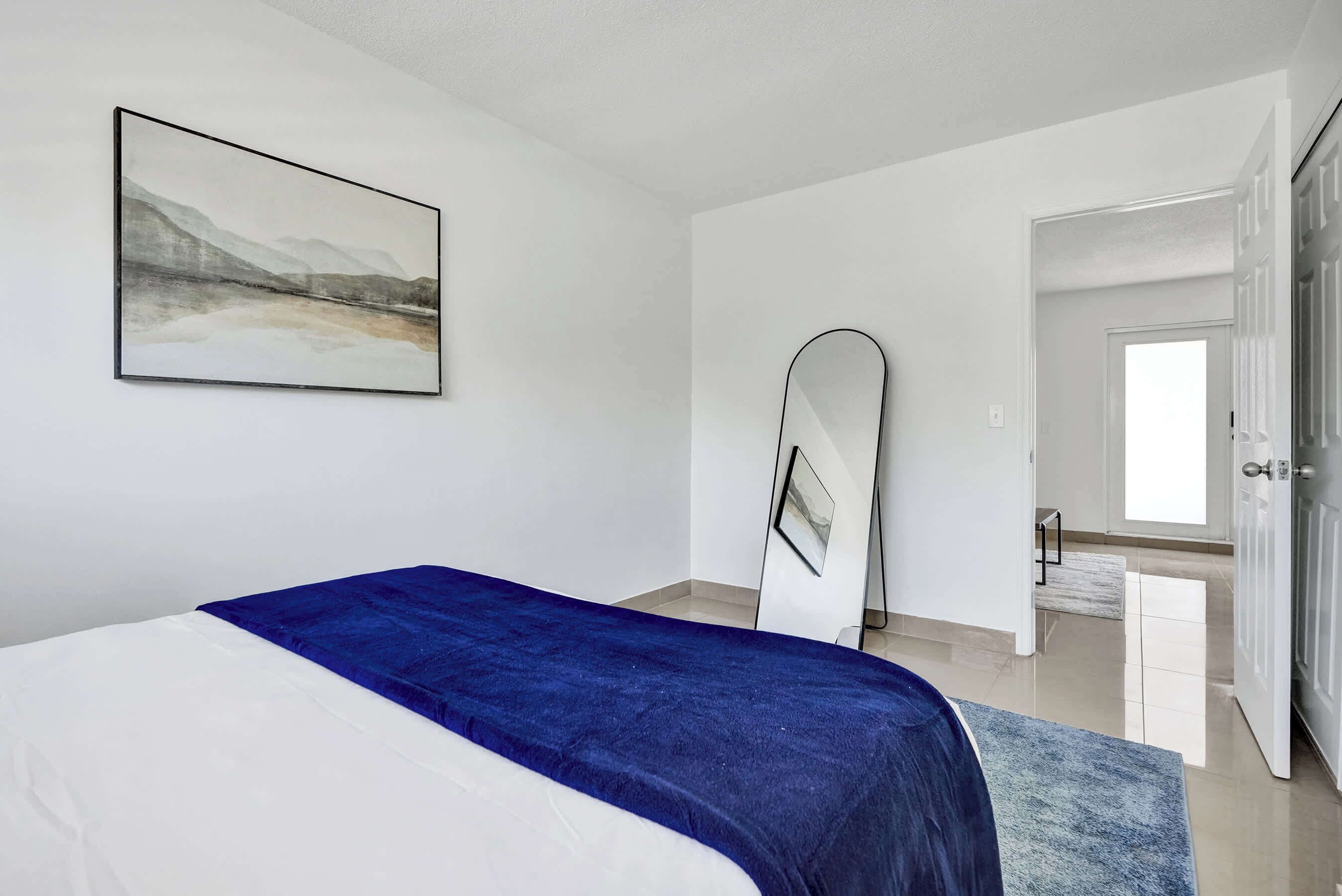 A bedroom with a bed, a large mirror, and a painting on the wall.