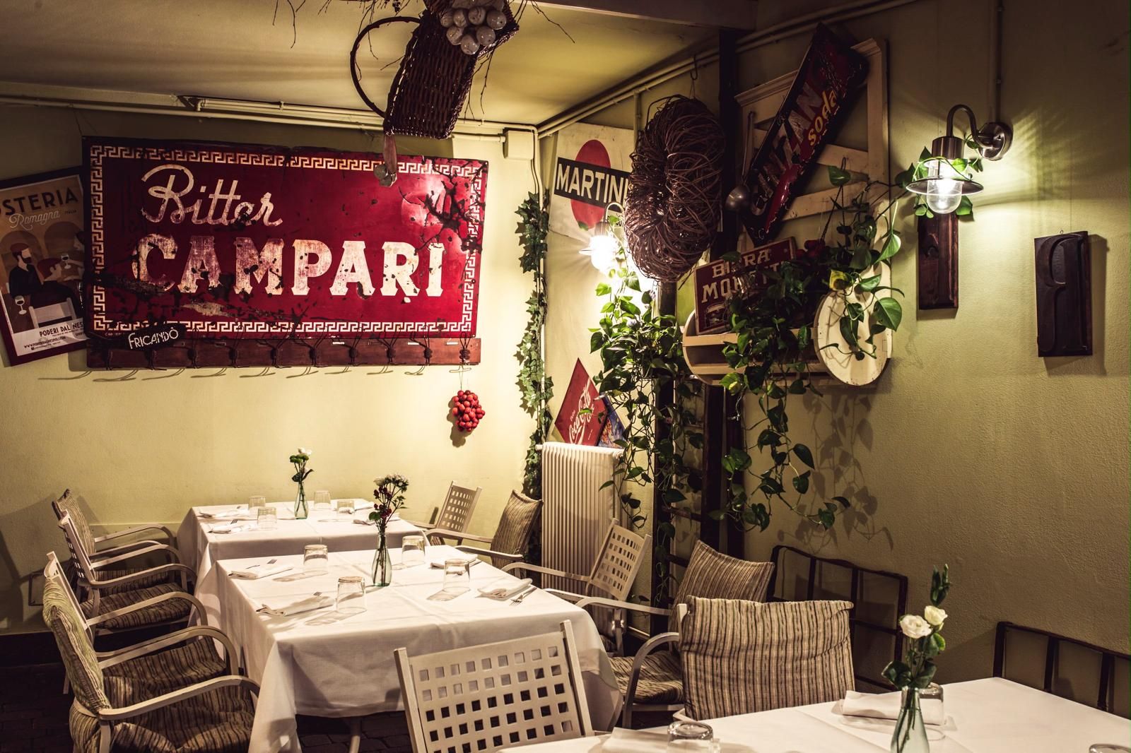 A restaurant interior with multiple tables set for dining, a hanging basket with fruits, and a large red sign with the restaurant's name.