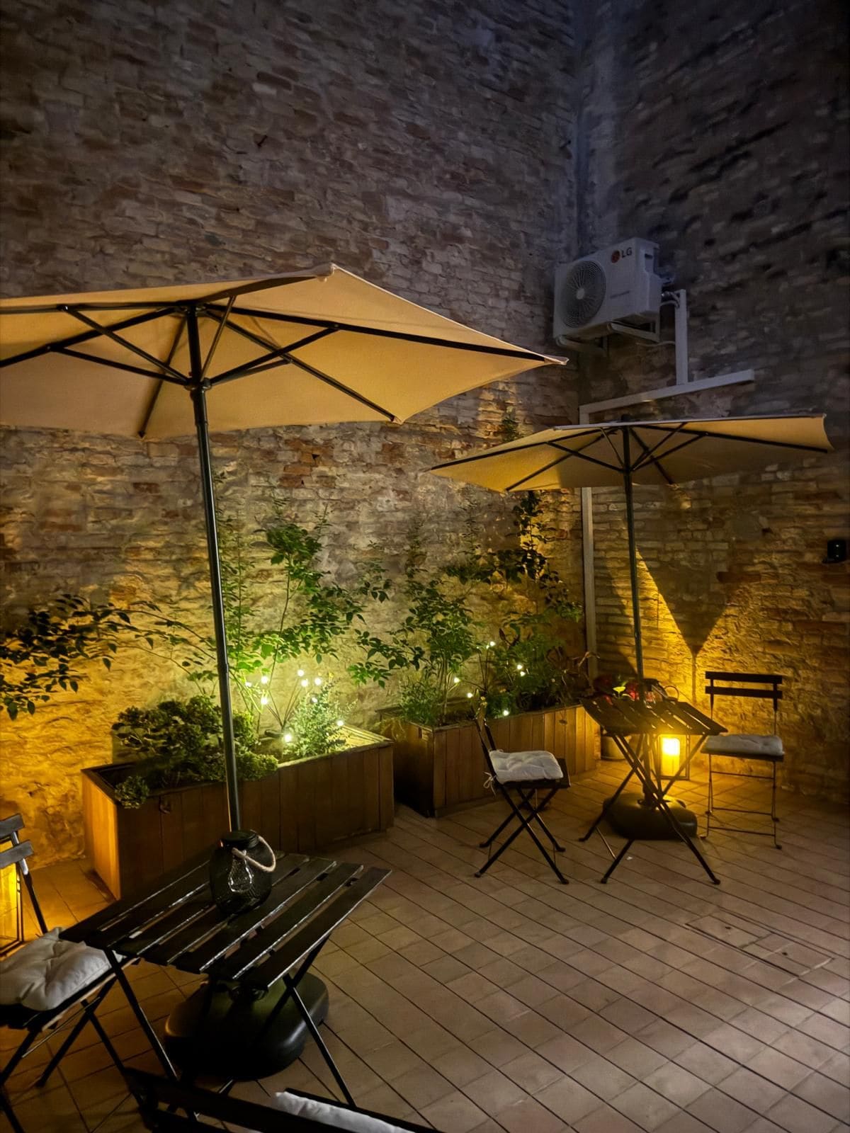 Un patio al aire libre con pared de ladrillo, mobiliario de madera y plantas en macetas.