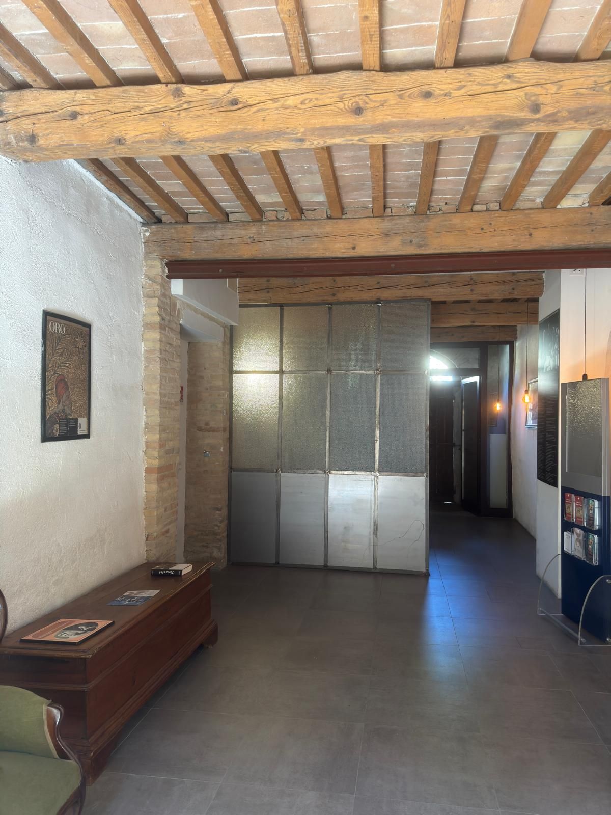 A hallway with a wooden ceiling, a bench, a wall-mounted picture, and a door leading to another room.
