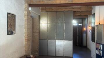 A hallway with a wooden ceiling, a bench, a wall-mounted picture, and a door leading to another room.