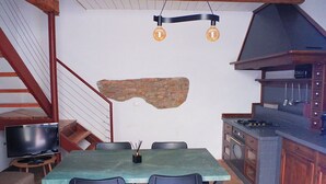 Un espace repas comprenant une table, des chaises, un téléviseur et une cuisine équipée d’une cuisinière et de placards.