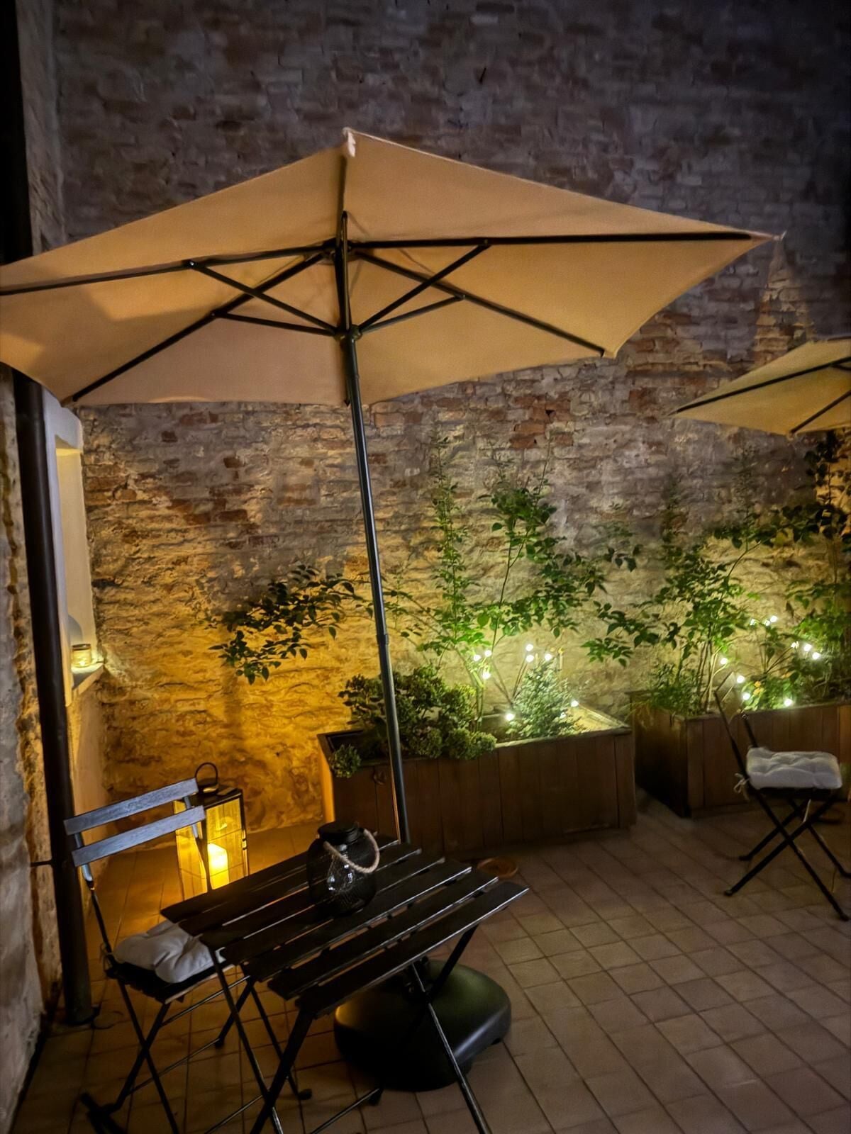 An outdoor patio with a brick wall, a wooden bench, a table, and two umbrellas.