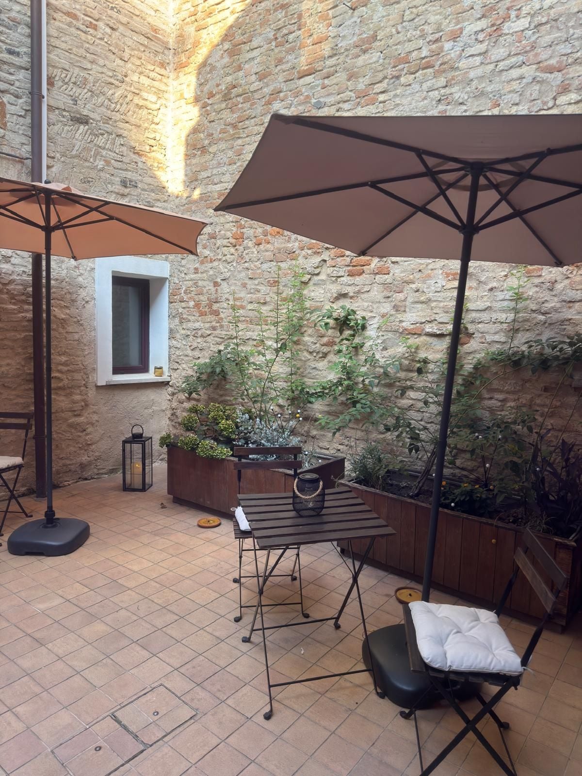 Een terras buiten met een bakstenen muur, een houten tafel, een bank en een grote parasol.
