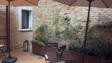 Een terras buiten met een bakstenen muur, een houten tafel, een bank en een grote parasol.