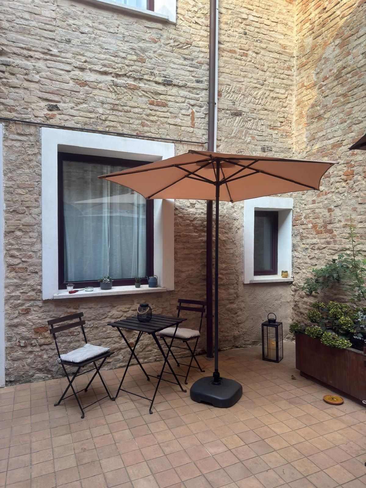 An outdoor patio with a table and chairs, a large umbrella, and a lantern.