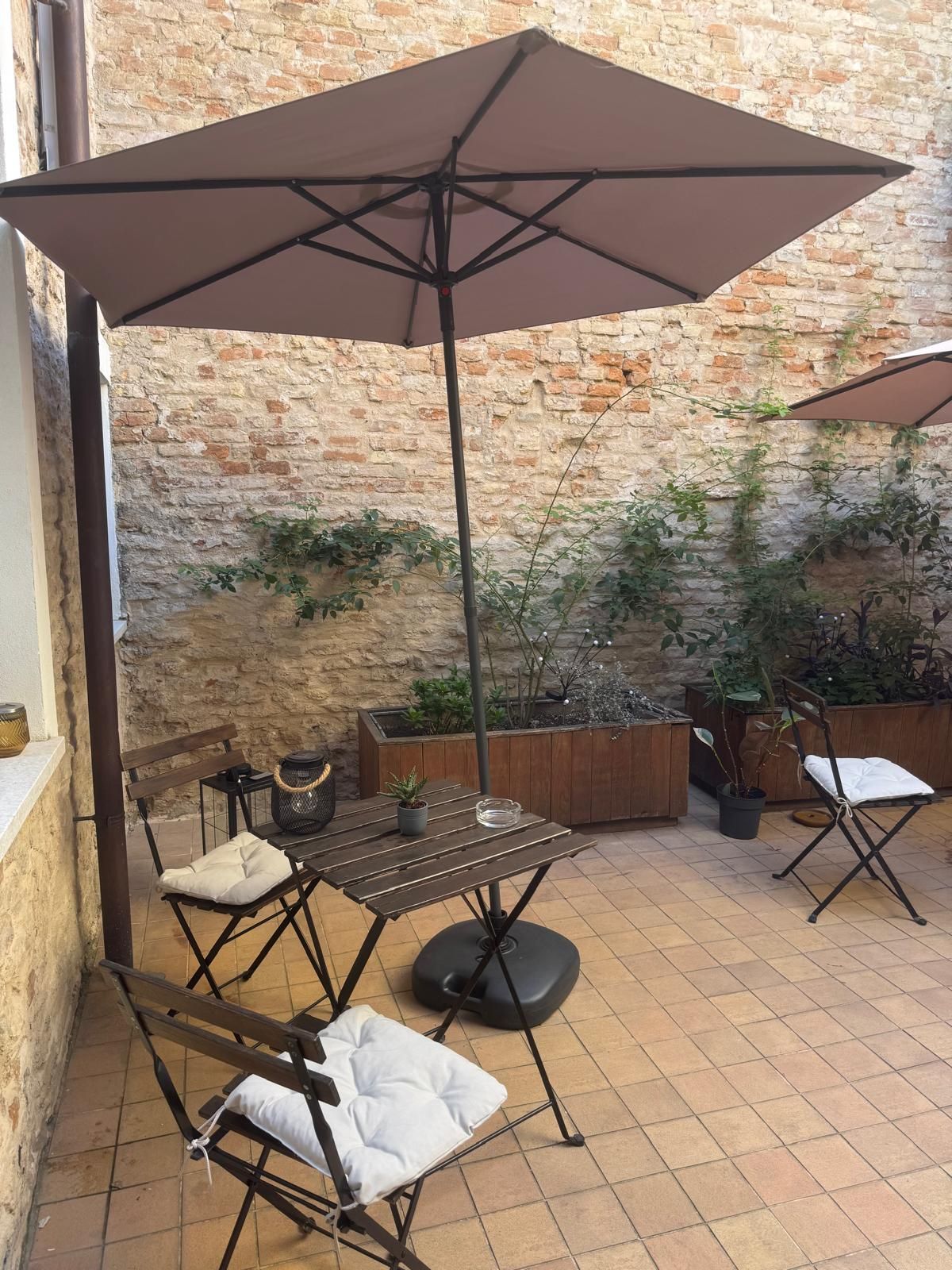 An outdoor patio with a brick wall, a table with chairs, and a large umbrella.