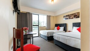 A hotel room with two beds, a desk, a chair, and a window with curtains.
