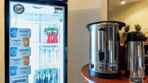 A refrigerator with a digital display, a coffee maker, and a kettle on a wooden table.