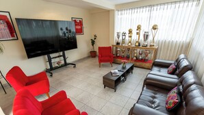 A living room with a flat-screen TV, red chairs, a brown leather sofa, a coffee table, and a trophy display.