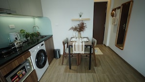 A compact kitchen with a washing machine, a dining table with chairs, and a mirror on the wall. - Hanoi Aurelia Stay (Hanoi)