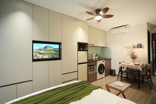 A compact hotel room with a bed, a small table, a washing machine, a ceiling fan, and a TV mounted on the wall. - Hanoi Aurelia Stay (Hanoi)