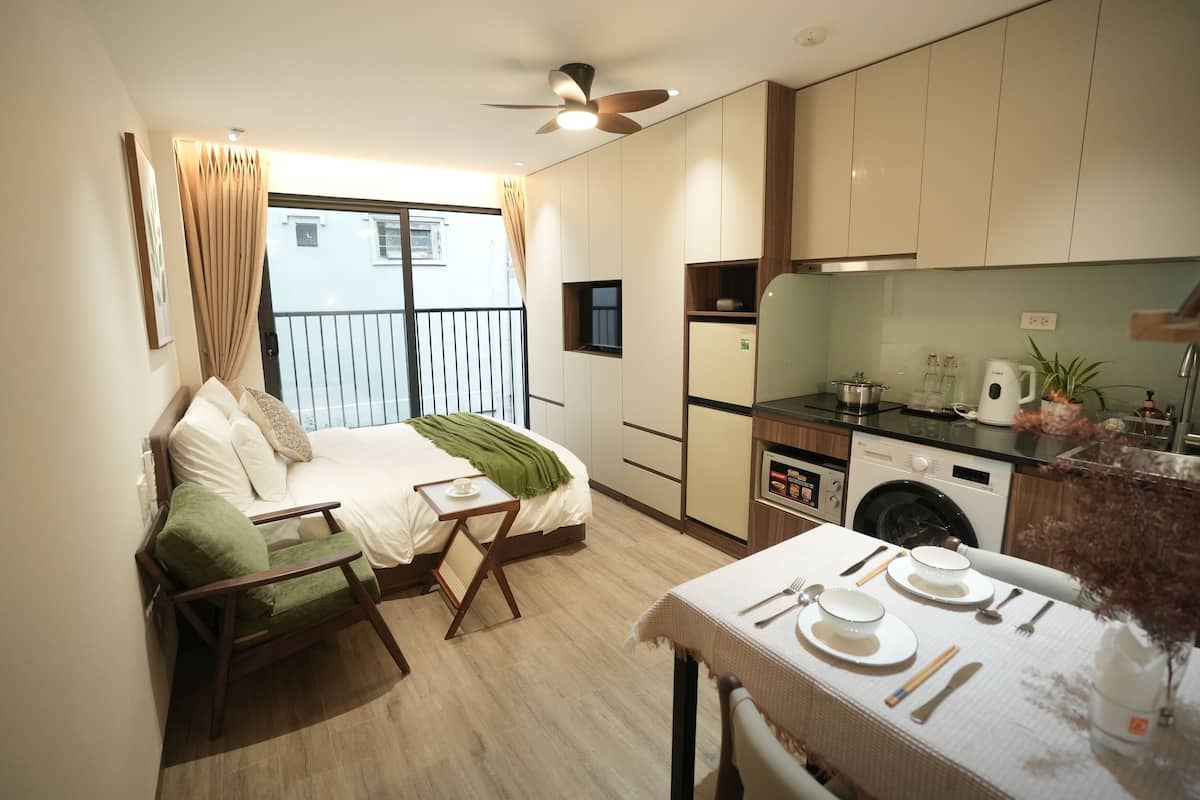 Un appartement moderne doté d’un balcon, d’un coin repas, d’une cuisine équipée et d’un lit avec une chaise verte.
