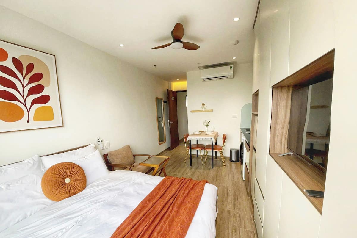 Une chambre d’hôtel comprenant un lit, un ventilateur de plafond, un appareil de climatisation, un coin repas avec une table et des chaises, et une fenêtre.