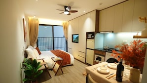 A hotel room with a bed, a dining table set for two, a kitchen area, and a balcony with curtains. - Hanoi Aurelia Stay (Hanoi)