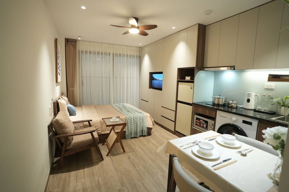 Une chambre d’hôtel compacte comprenant un lit, une petite table à manger, un coin cuisine et un ventilateur de plafond.