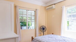 Una stanza con un letto, una finestra con tende, un condizionatore d'aria e una ventola da terra.