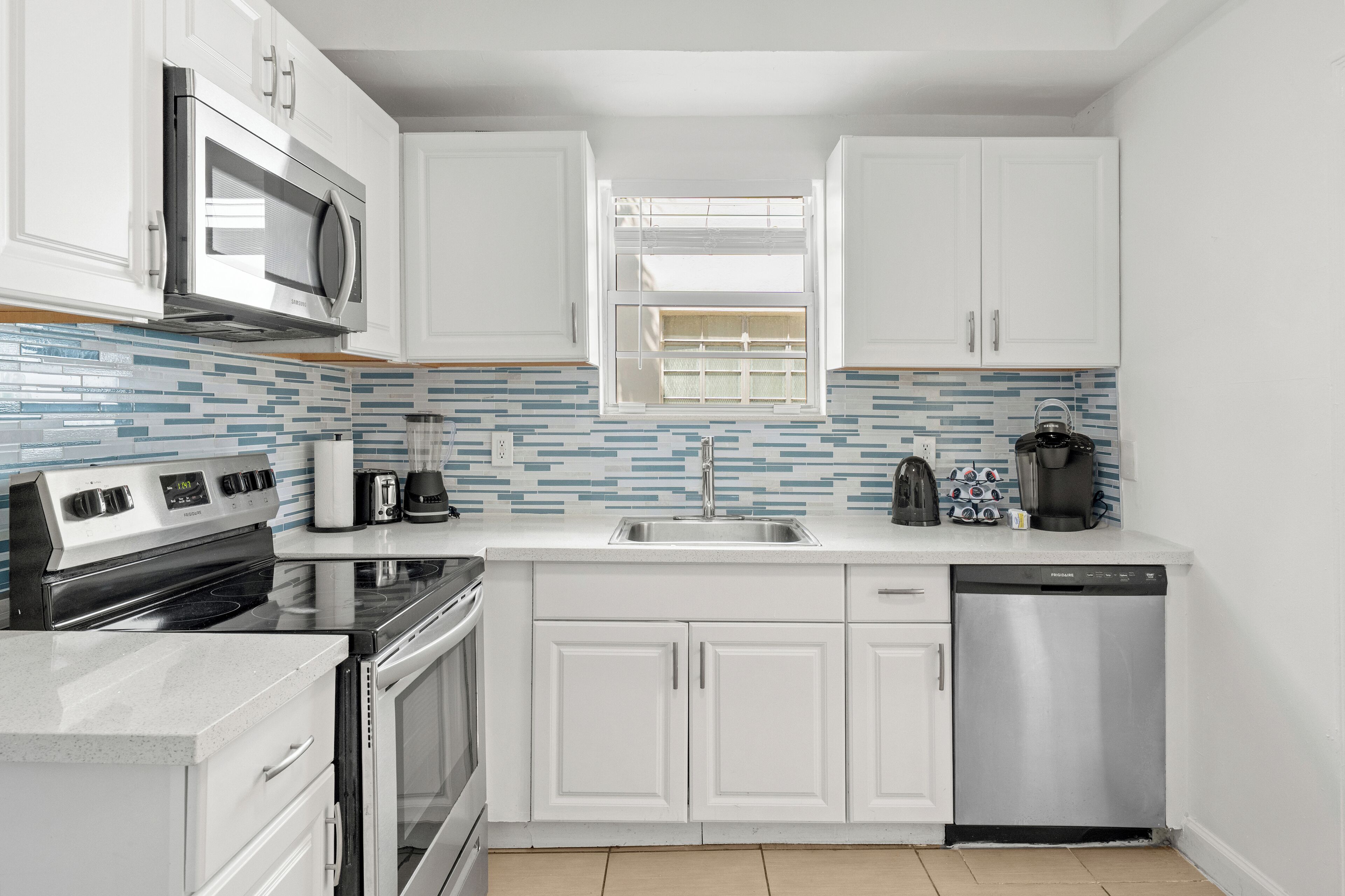 A modern kitchen with white cabinets, a stainless steel dishwasher, and a microwave.