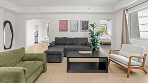 Un salon moderne avec un canapé d’angle, un fauteuil vert, une table basse en bois et un canapé blanc.