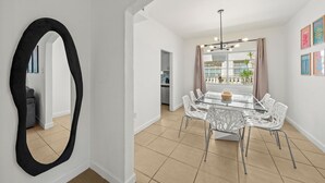 Un espace repas moderne avec une table en verre, des chaises blanches et un miroir noir.