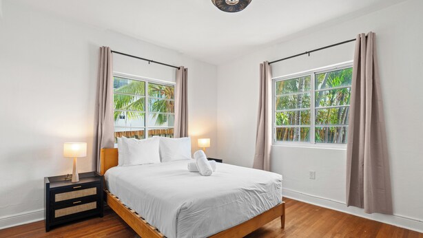 Une chambre avec un lit en bois, une table de chevet avec une lampe et une fenêtre avec des rideaux.