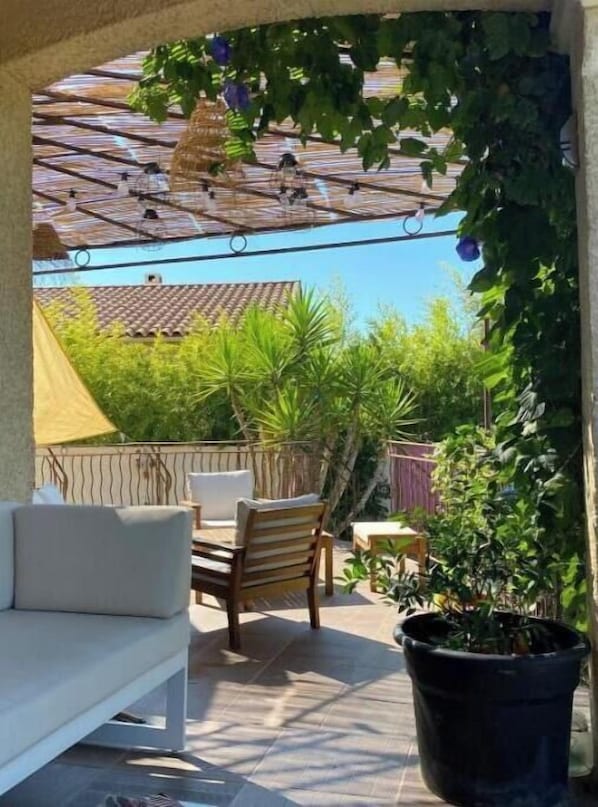 A patio with a white sofa, a wooden chair, a table, and a potted plant.